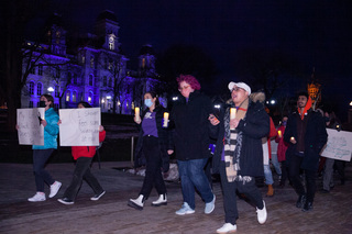 Crowds of people march past the Hall of Languages displaying signs and holding candles. 